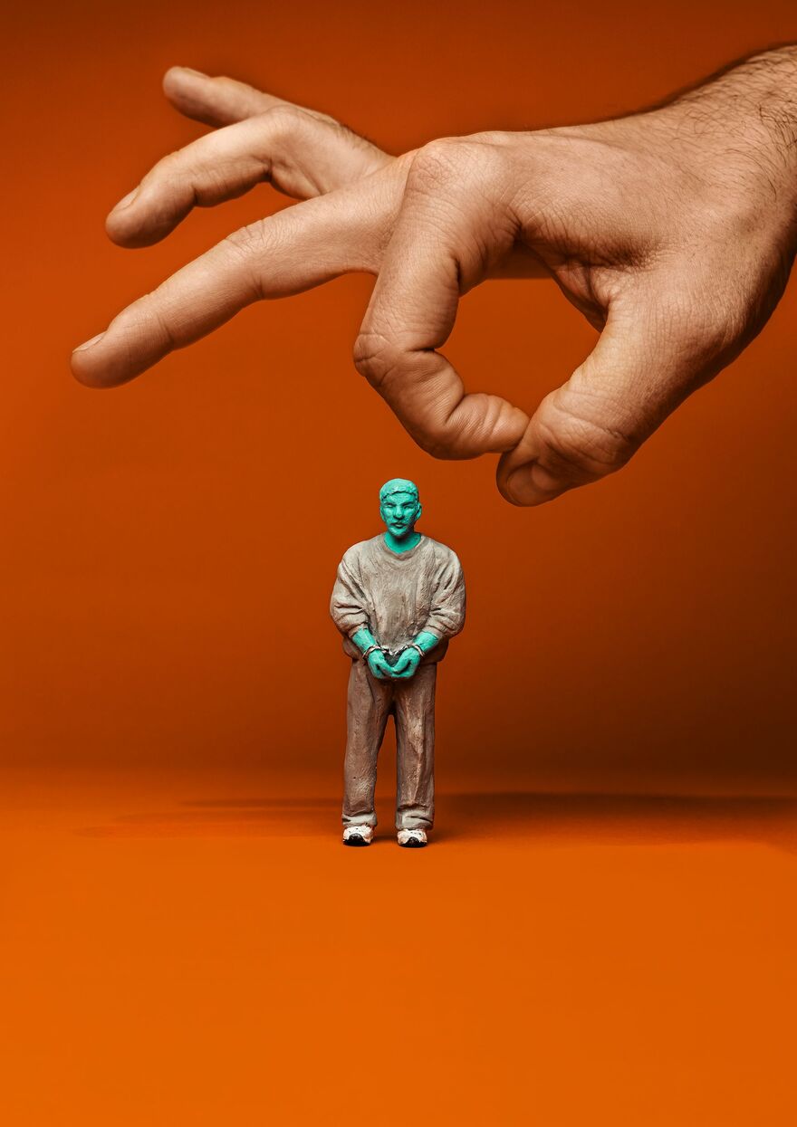 A bright green action figure standing in beige tracksuit against a orange background. A large hand is about to flick him