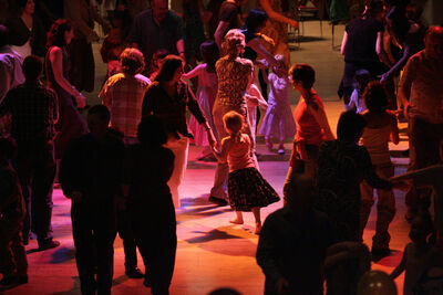 Lots of people of different ages dancing in a dimly lit room with orange, purple and pink lights