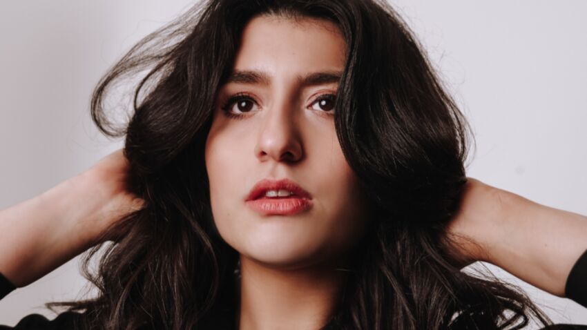 A woman with long dark brown hair has her hands resting behind her head