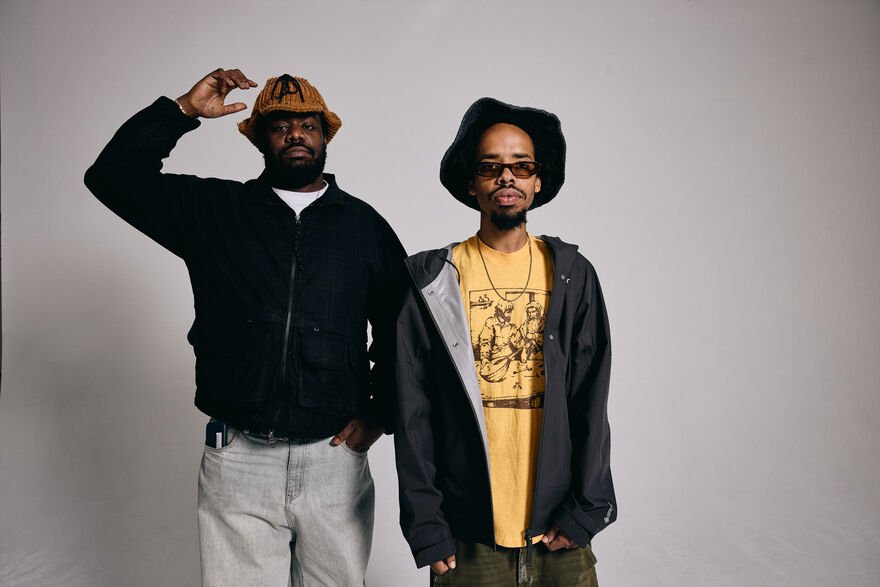 Earl Sweatshirt and MIKE both wearing bucket hats and zip up hoodies standing in front of a grey background