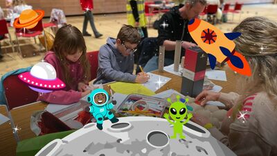 Children crafting on a table with pencils and cardboard. There are cartoon space ships, UFOs and aliens placed over the image