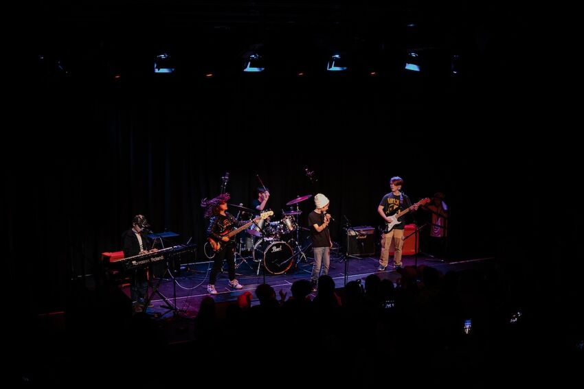 A group of young musicians on stage. They are performing as a band with a drum kit, guitars and a lead vocalist