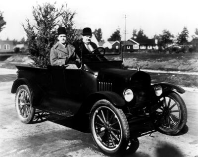 Old black and white photo of an old car with two men in top hats sitting inside