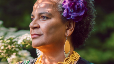 Akila Richards with a flower in her hair looking off into distance. 