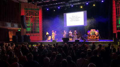 Ida Green, a live band an an organ onstage at Brighton Dome in front of a large standing crowd. A screen behind has lyrics displayed for 'Last Christmas'