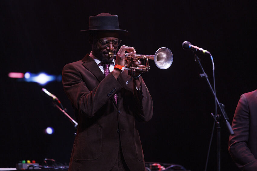 Mark Kavuma playing the trumpet in a suit and hat