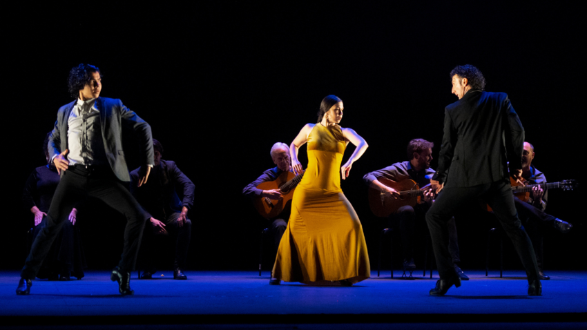 Woman in yellow dress and two men in suits dancing in front of acoustic guitarists