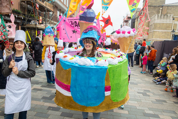 A white child with brown hair stands in the middle of a colourful papier mache cake