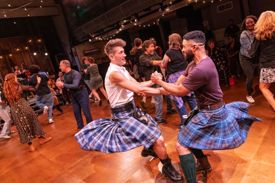 Hall of people dancing. Two men in kilts are spinning around in a circle together holding hands.