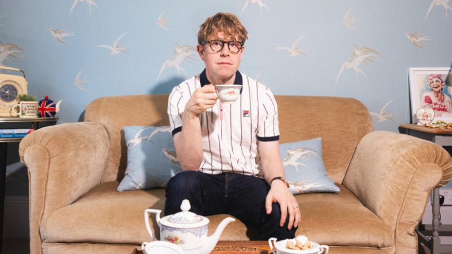 Josh Widdicombe sat on a sofa holding a cup of tea