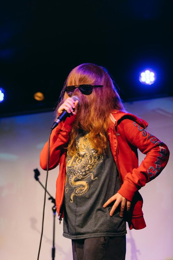 A young person on stage speaking into a microphone with their hair over their face and their glasses over their hair