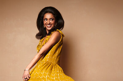 A woman wearing a gold dress, she is smiling and looking to the right