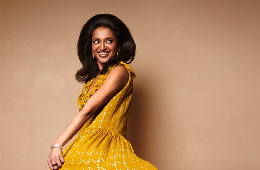 A woman wearing a gold dress, she is smiling and looking to the right