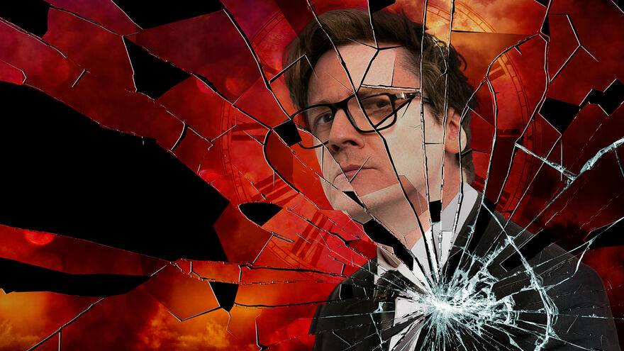 man with glasses in a suit is situated in a red/ amber backgound which has a shattered glass effect