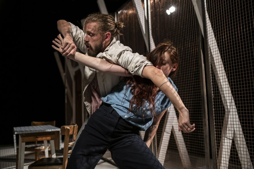 A man and woman on stage, the man is holding the woman's arms away from her in a dance sequence position