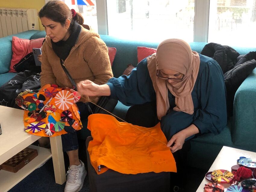 Two women work embroidering a bright and colourful tapestry