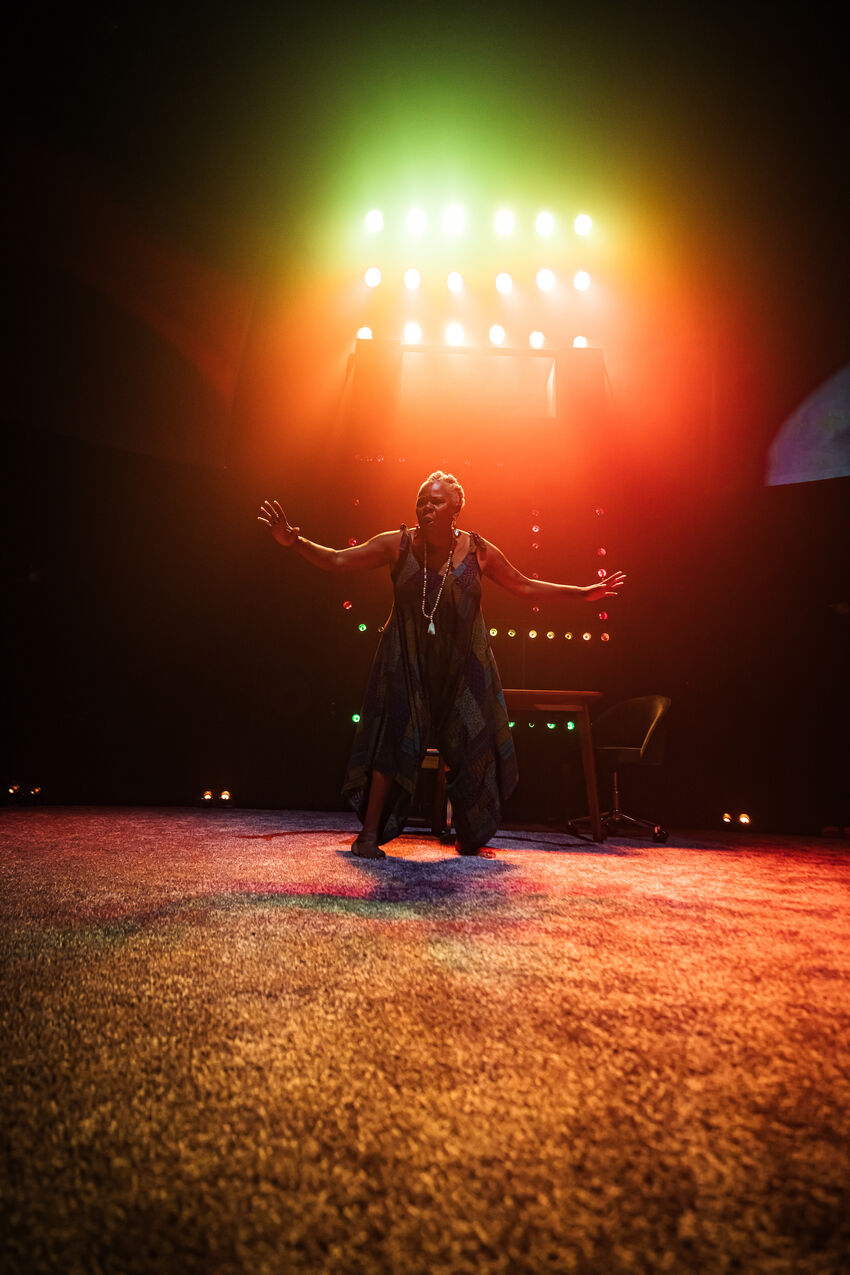A woman holding her arms up, standing in front of orange and green spotlights