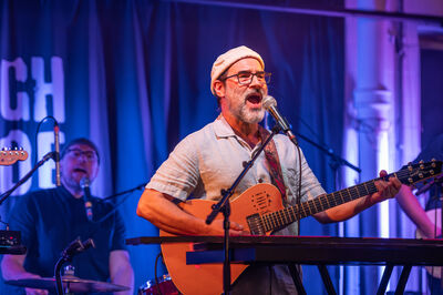 Adam Buxton playing a guitar and singing on stage