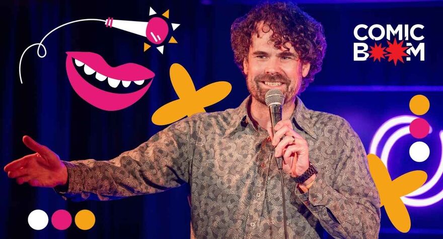 A man wearing a shirt on stage with a microphone. He is surrounded by pink and yellow graphics