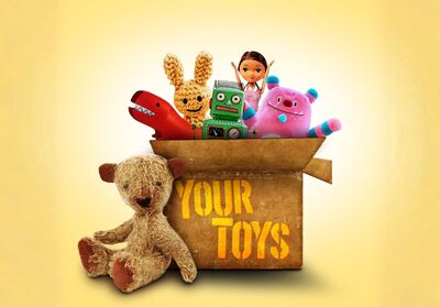 Multiple toys in a cardboard box with 'Your Toys' written on the front. Sat next to the box is a brown teddy bear