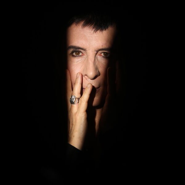 Marc Almond looking dramatically at camera with his hands on his face, mostly in shadow