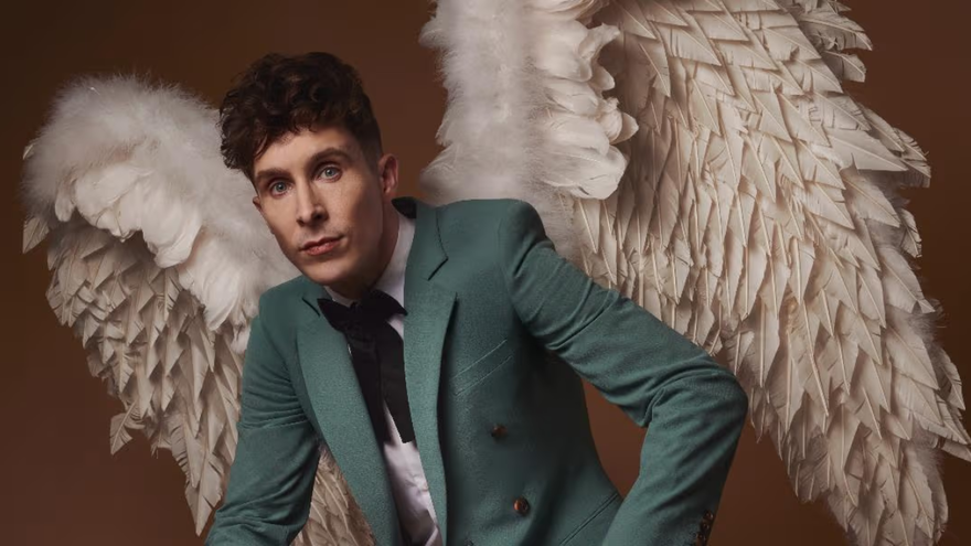 Larry Dean wearing a turquoise suit and black tie with angel wings made of feathers
