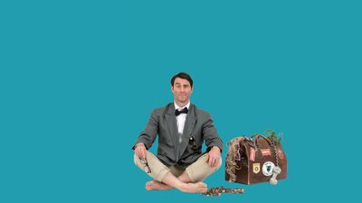 Jimmy Rees sat cross legged wearing a blazer and black bow tie. He is sat next to some chain and a going away bag with hair coming out. He is in front of a plain blue background