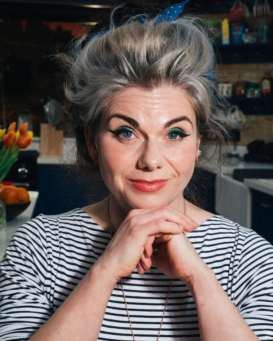Photograph of Caitlin Moran wearing a stripy top from the shoulders up with her chin resting on her hands