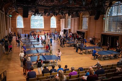 Big hall with lots of table tennis tables and people playing
