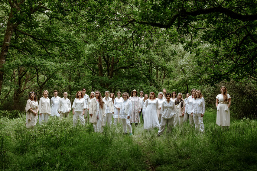 A large of people all dress in white clothing, standing in a green forest