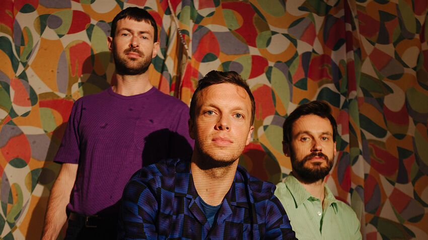 three men look forwards and downwards with a neutral facial expression situated within a colourful and patterned background