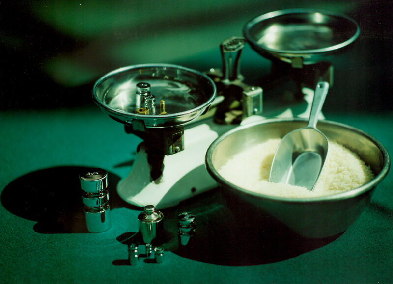 Old fashioned weighing scales sat next to a metal bowl of rice, with a metal scoop in it.