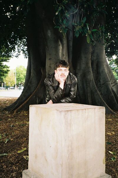 Ed Night leaning on his hand against a concrete cube. He is standing in front of a big tree
