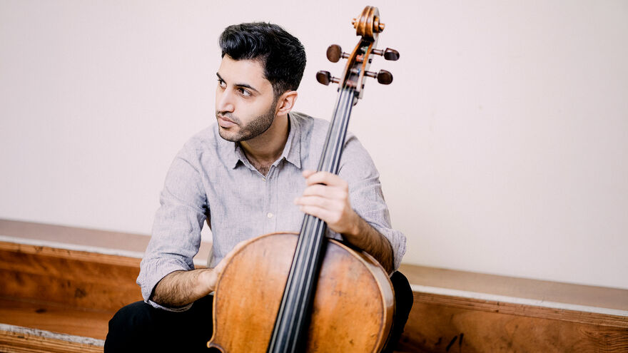 Kian Soltani sits holding his cello and looking into the distance