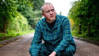 Miles Jupp crouching down in the middle of a country lane