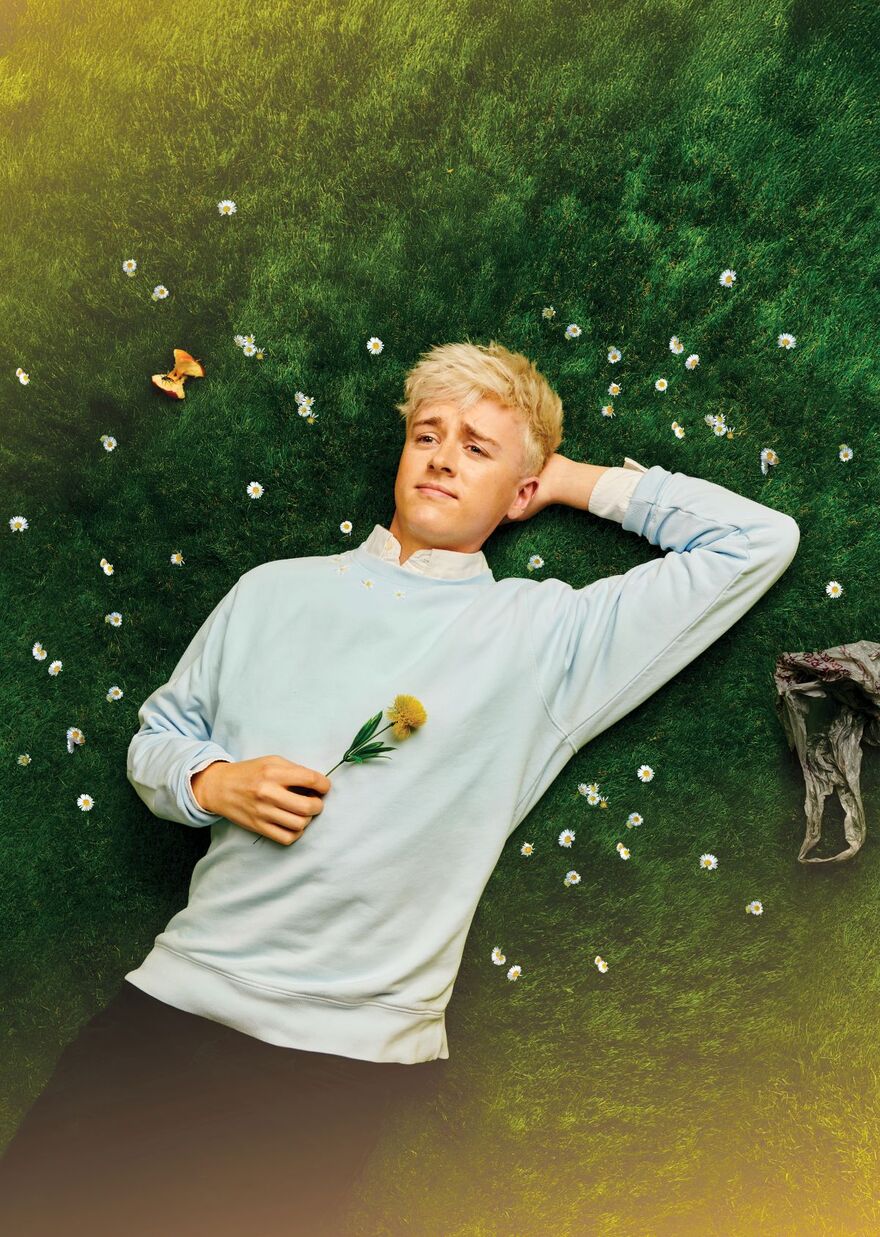 Daniel Foxx lying down on grass with their arm behind their head and holding a flower