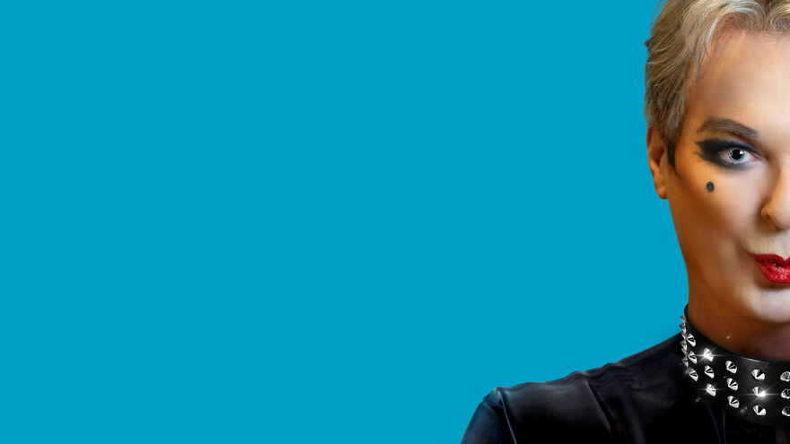 Julian Clary wearing dark eyeshadow pouting. Half their face is cut off out of the picture