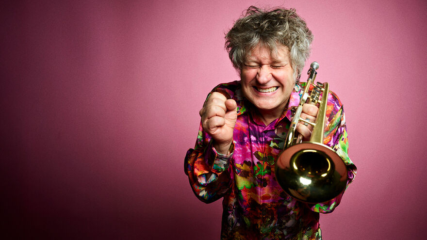 Image of man holding trumpet wearing a flowery shirt with an excited expression on his face as he holds his fists up