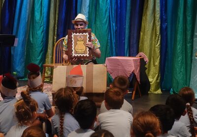 An actor holds up a drawing of a woman sat inside a vinegar bottle to a group of primary school children