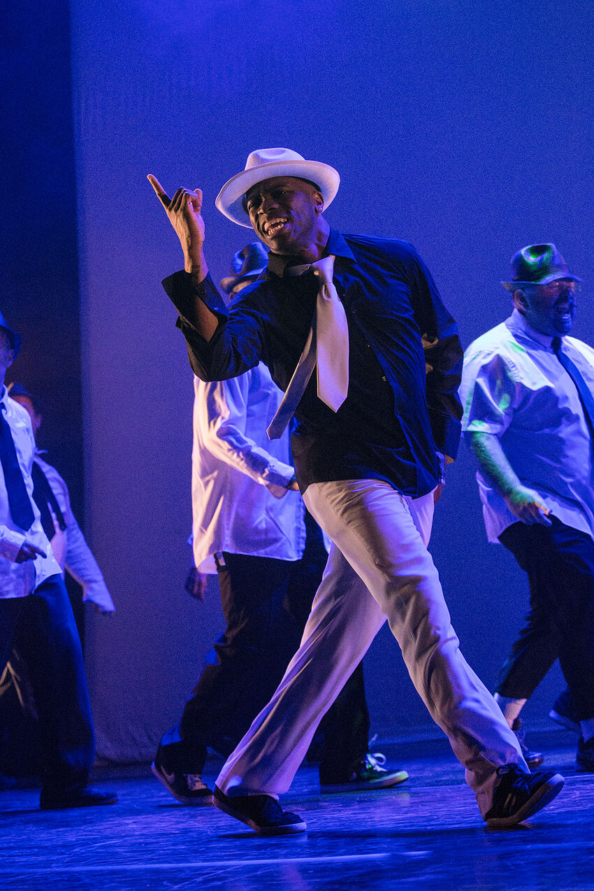 Dancer OP Omari in a hat and tie dancing in front of a blue backgroun
