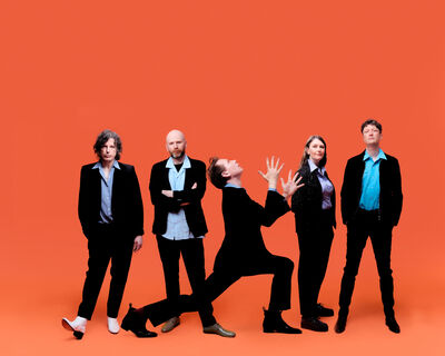 Franz Ferdinand standing in black and blue shirts in front of a orange background