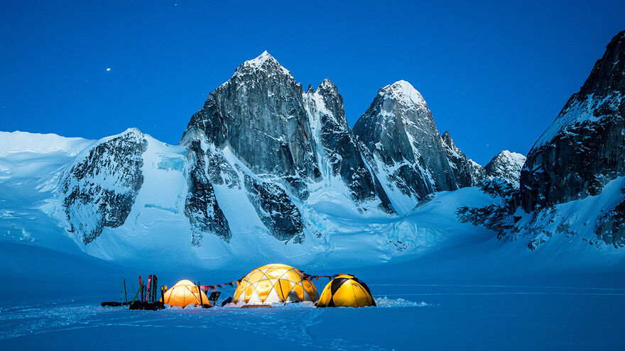 Three tents pitched in the snow in front of snow topped mountains