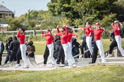 A group of 8 girls dancing in red, black and white outfits. They are in a skatepark.