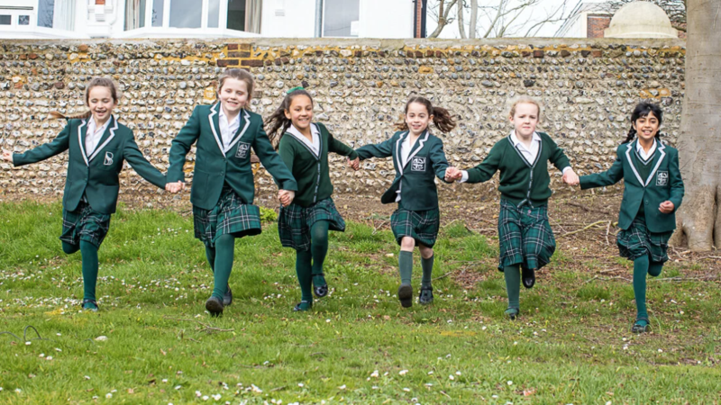 6 young girls in green school uniform running towards the camera, all holding hands