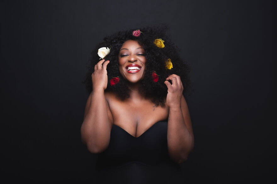 Judi Love in a black dress with yellow, red and white flowers in her hair