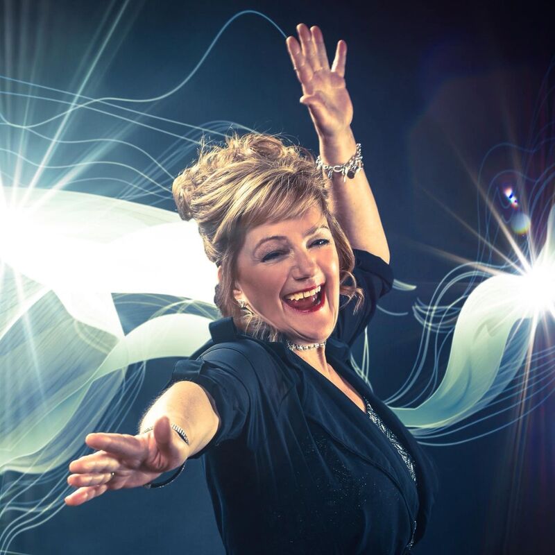 Nicki French smiling with one hand in the air and light patterns behind her