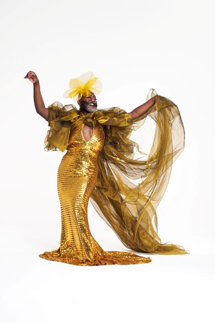 Le Gateau Chocolat smiles in a shiny gold statuesque dress with gold tulle ruffles and a train