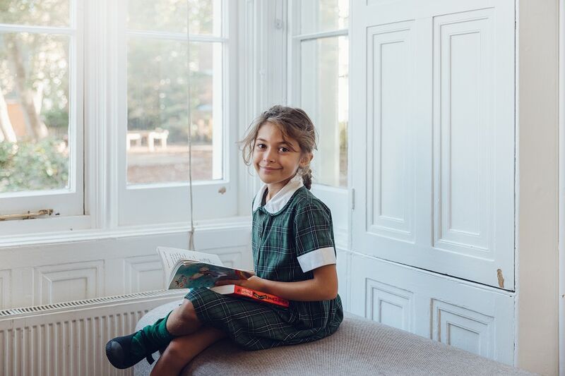 A school child in school uniform sat on a sofa reading a book