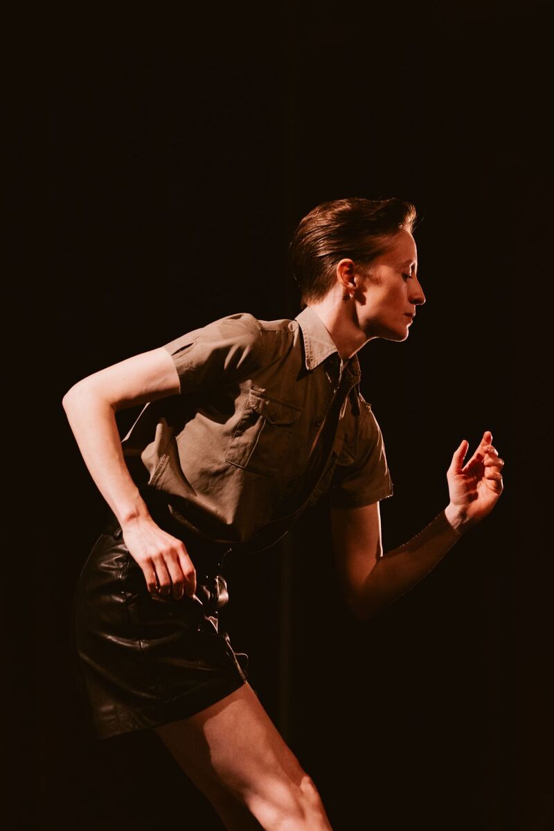 A profile picture of a dancer standing with their arms in opposite angles, they have short gelled back hair and are wearing shorts and a short sleeved button up