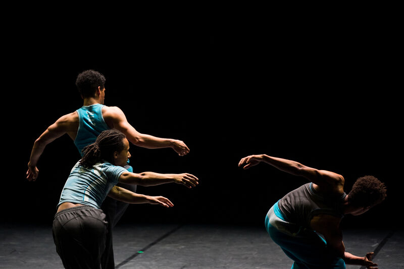 Three male dancers move fluidly on a stage